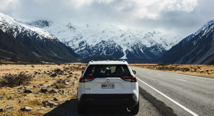Carro branco em uma estrada com cenário de montanhas com gelo ao fundo
